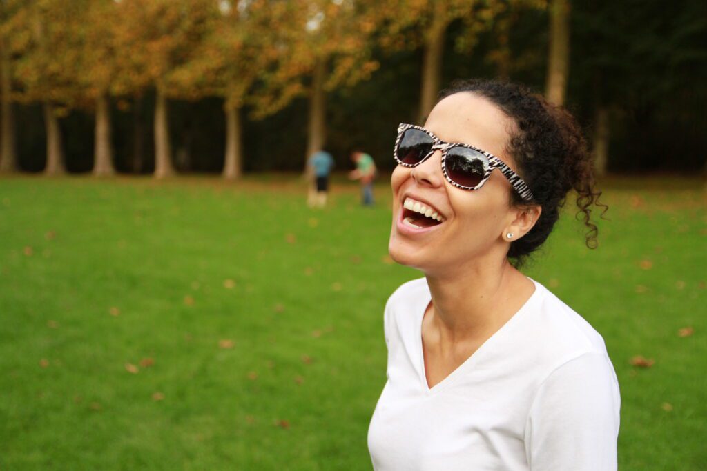 Sobre Mim Foto de mulher rindo num parque com óculos de sol. Ingrid Veríssimo