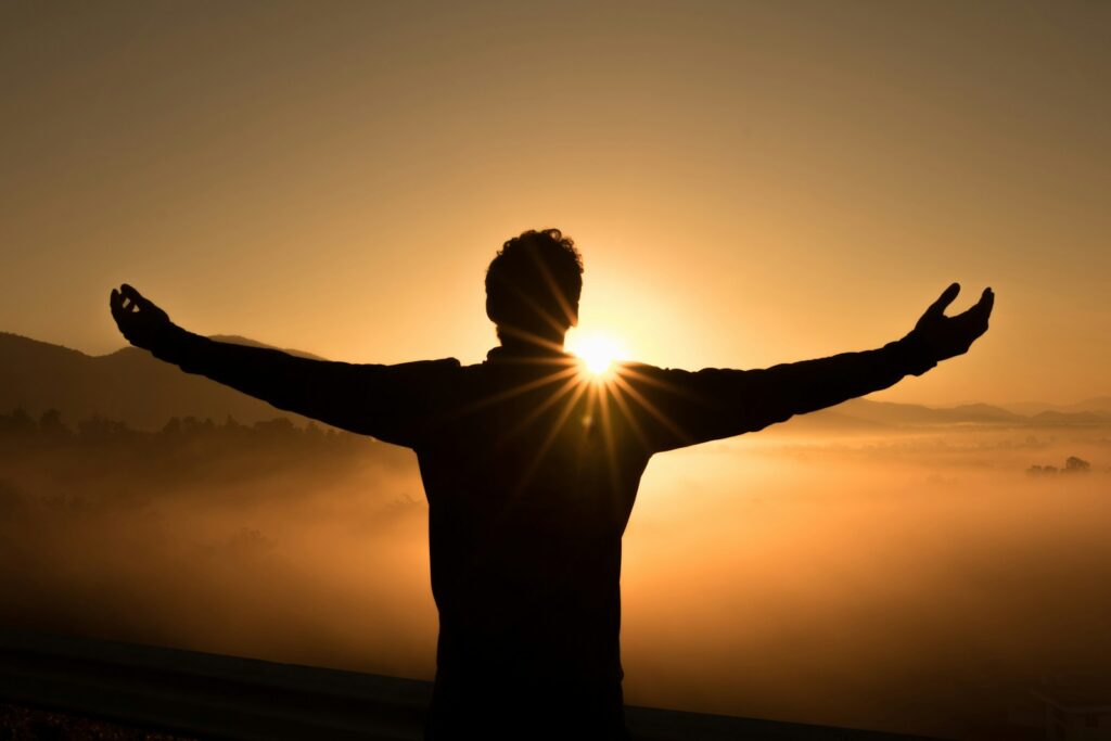 Buscar Deus: De Onde Vem Essa Vontade? Silhueta de um home abrindo os braços no nascer do sol. Buscar a Deus