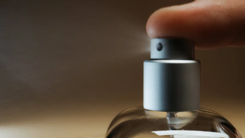 Detalhe do dedo apertando uma válvula de spray de perfume com ingredientes controversos